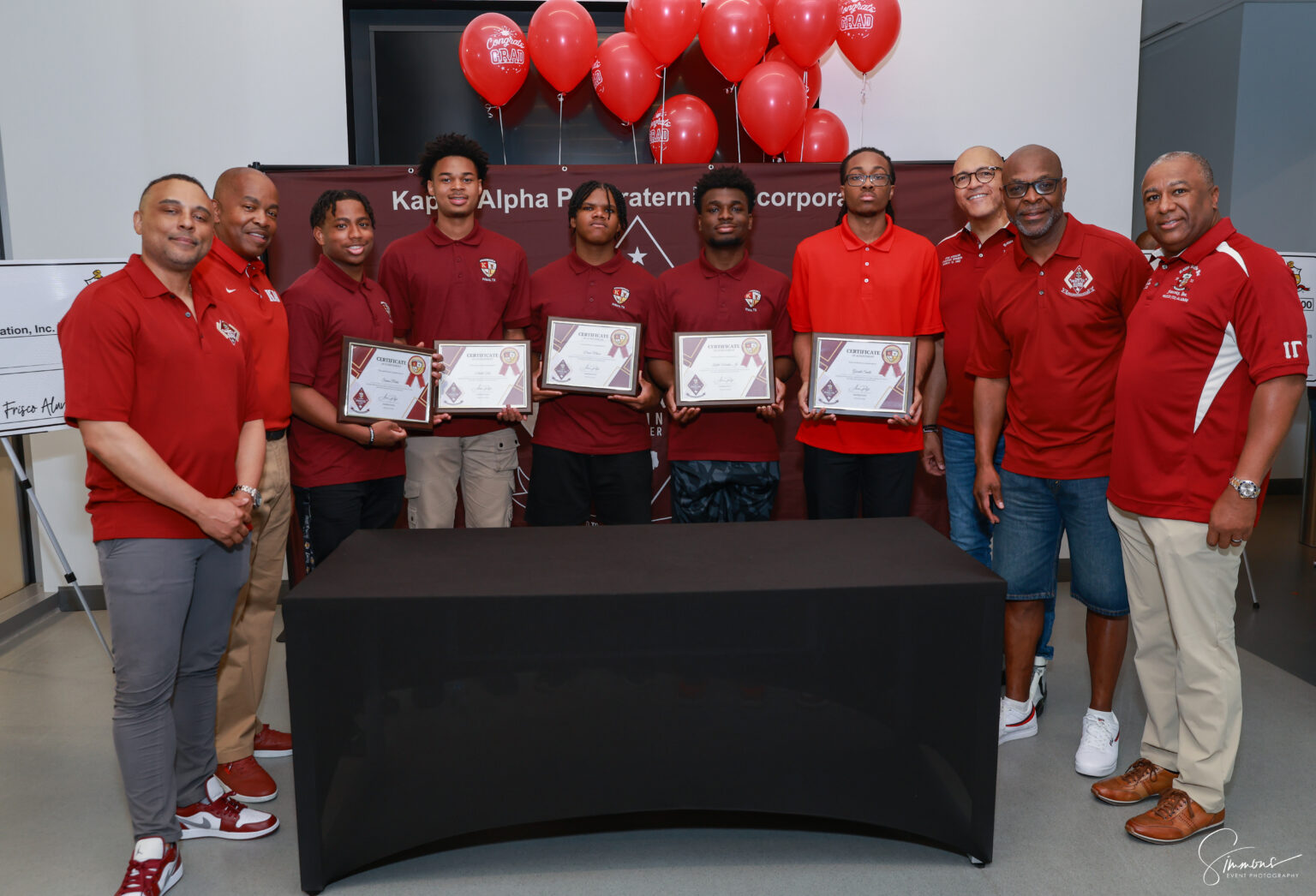 A group of men holding certificates in front of balloons.