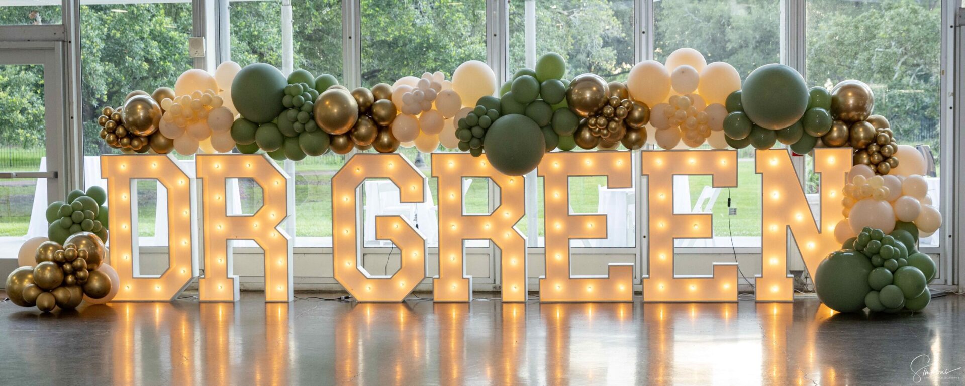 A large lighted sign with balloons and greenery.