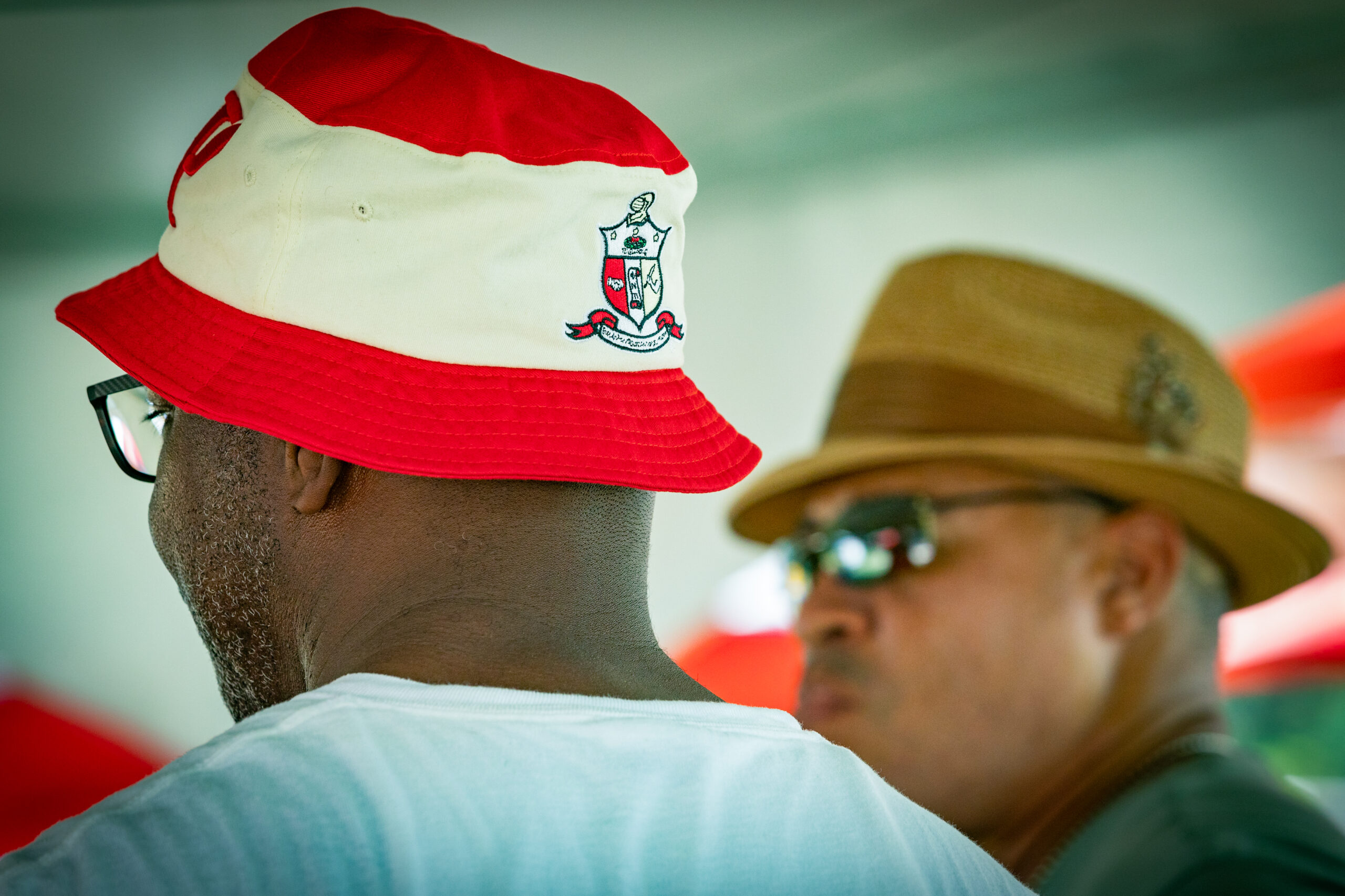 Two men wearing hats and sunglasses talking to each other.