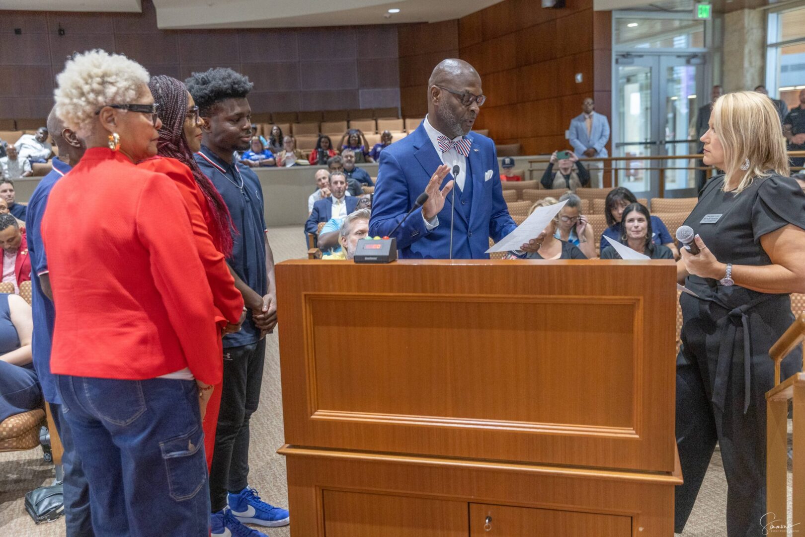 A man in blue jacket standing at podium with people.